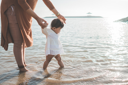 portrait of a mother help her daughter by holding her hand walking on the beach for the first timeの写真素材