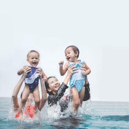 two babies having fun in the swimming pool with their motherの写真素材