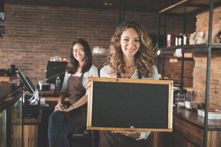 portrait of attractive female waitress standing and holding blank blackboard sign at a cafe