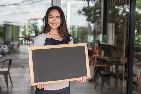 happy small business owner ready to open her cafe for the first time. holding chalk boardの写真素材