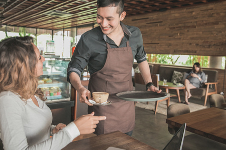 portrait of a male waitress serving coffee to a female customerの写真素材