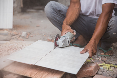 worker cutting a tile using an angle grinder at construction siteの写真素材