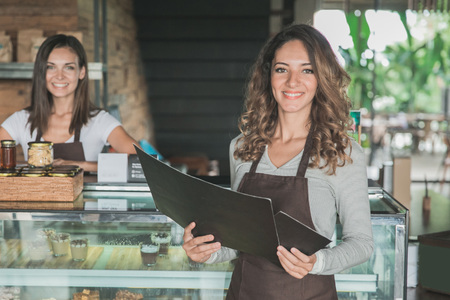 attractive waitress smiling to camera and holding a menuの写真素材