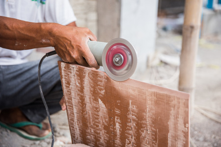 worker cutting a tile using an angle grinder at construction siteの写真素材