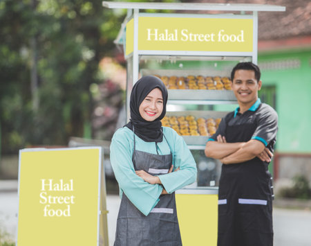 young asian muslim small food stall owner, standing proudly with her partner at the background. halal street food conceptの写真素材