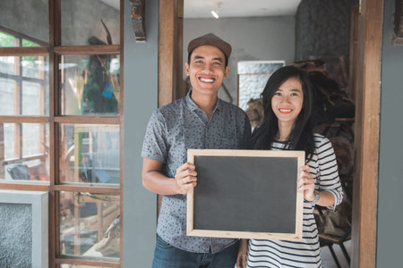 portrait of two business owner holding a blackboard in front of their shopの写真素材