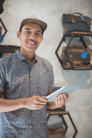 portrait of asian male business owner standing in front of his bag store with tabletの写真素材