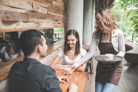 portrait of a female waitress serving coffee to a couple customerの写真素材
