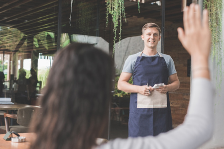woman is calling the waiter in cafe. she is raising her armの写真素材