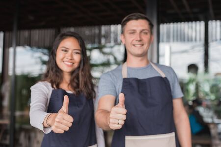 two waiter showing thumb up together while standing in front of their cafeの写真素材