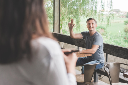 man is calling the waiter in cafe. He is raising his arm and smilingの写真素材
