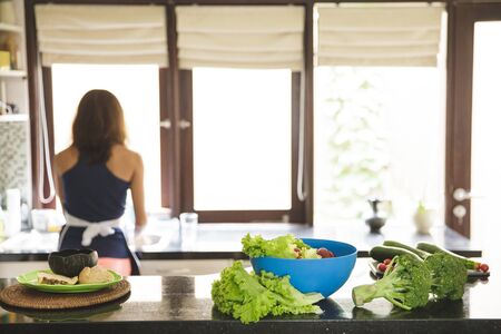 portrait of vegetables on tables at kitchen with housewife at the background with copy spaceの写真素材