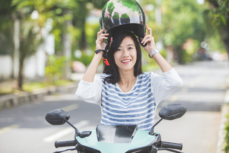 happy asian woman put helmet on before riding a motorbikeの写真素材