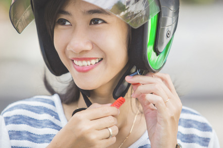 happy woman fastening her motorbike helmet in the city streetの写真素材