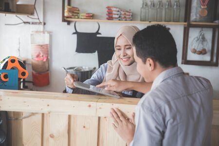 portrait of asian muslim female waitress showing cafe menu to her cutomerの写真素材