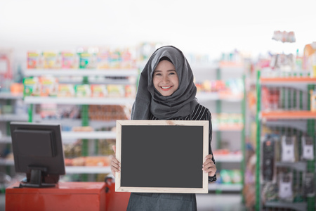 asian muslim woman standing in front of the store showing blank black board. halal business conceptの写真素材
