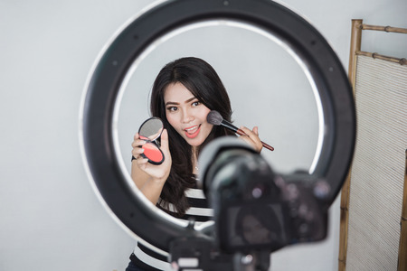 beauty blogger. makeup tutorial. video blog concept. portrait of asian woman showing makeup tutorial online using camera and lighting equipmentの写真素材
