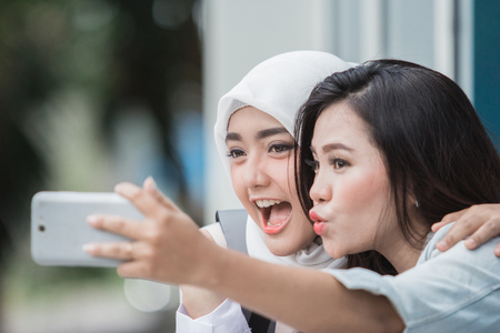 two asian young student taking selfie together with smartphone on campusの写真素材