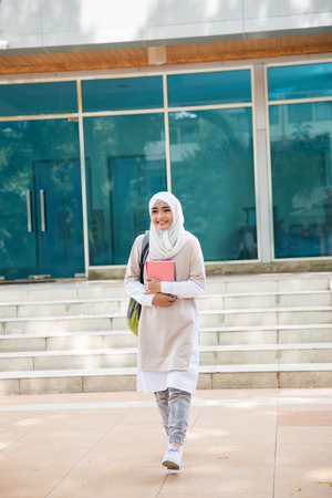 cheerful asian female university students wearing head scarf walking on campusの写真素材