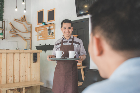 asian coffee waiter holding tray with coffee delivering to customerの写真素材