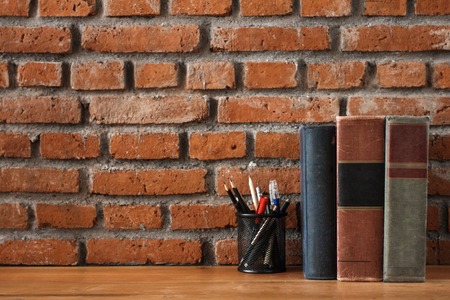 books and stationary supplies on wooden table with brick wall baの写真素材