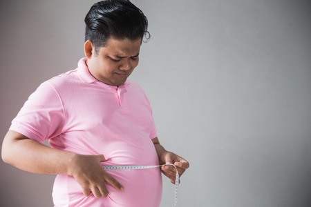 Young fat man measure his bellyの写真素材