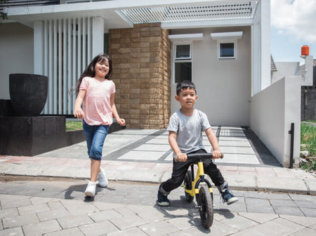 kids ride bicycle and sister running behind him