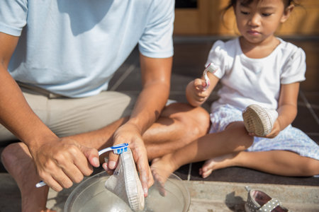 father with her toddler girl washing their shoes together