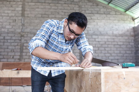 young carpenter measuring and marking the wood boardの写真素材