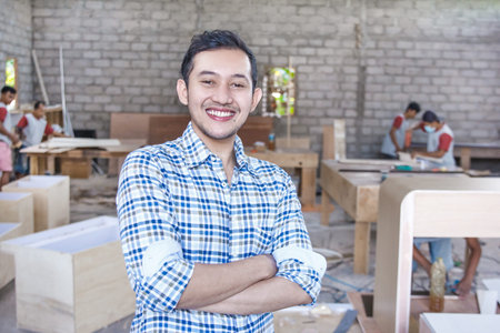 young carpenter smiling with arm crossed at carpenter workshop
