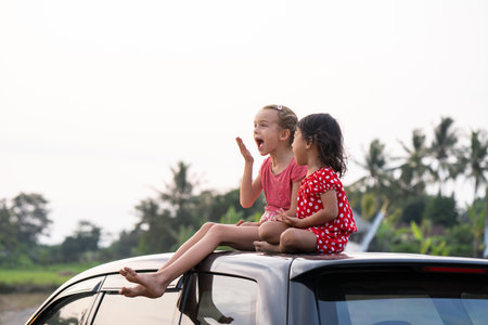 two happy young kid sitting on top of the car and playing