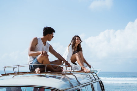 young couple with sunglasses sitting on top of minivan roof