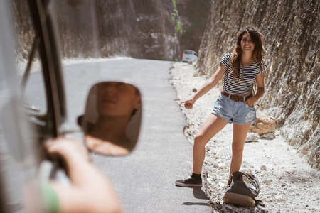 Beautiful hippie woman standing on a road with thumbの写真素材