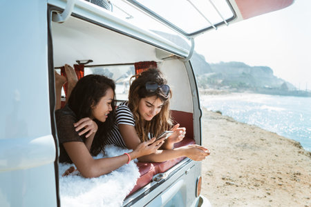 two young woman lay down hold smartphone inside of retro vanの写真素材