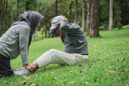 old man doing sit up in the park with wifeの写真素材