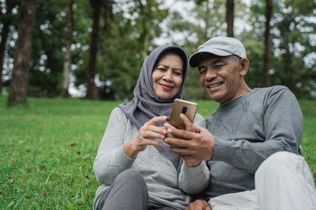 senior muslim couple using smartphone together in the parkの写真素材