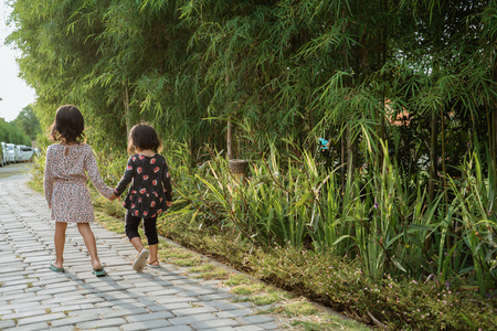 from side view portrait  of two little girl holding hands each other walking leaving a park in the afternoonの写真素材