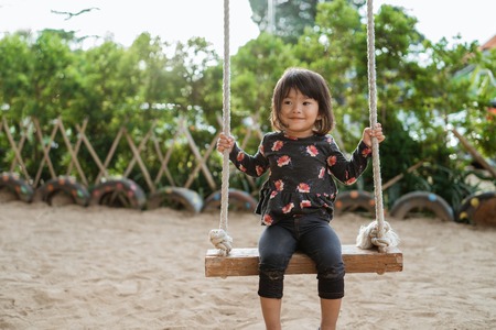 asian little girl enjoying playing a swing alone at the parkの写真素材