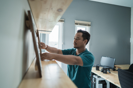 portrait of young man worker arranging wall decorationの写真素材