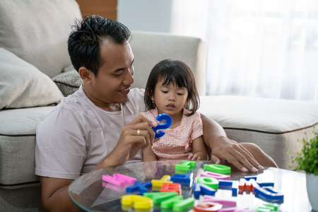 portrait of a patient father teaches the alphabet to his daughter by playing colorful text toysの写真素材