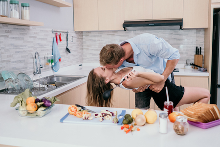 young happy couple hold hands and kissing when prepare for cookingの写真素材