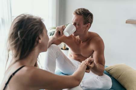 young romantic couple sitting on bed and having a cup of coffeeの写真素材