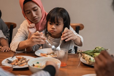 muslim mom eat with her daughter sitting on lapの写真素材