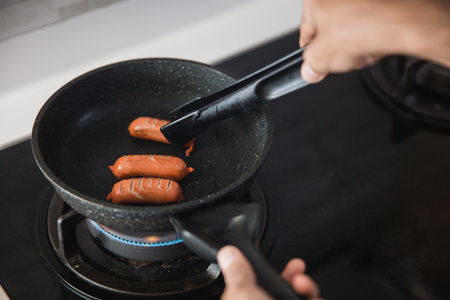 hands using food tongs to frying sausagesの写真素材
