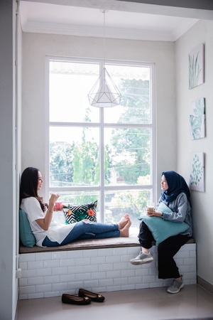 muslim woman and asian friend sitting by the windowの写真素材
