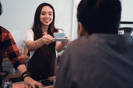 asian barista served cup of coffee in cafe to customerの写真素材