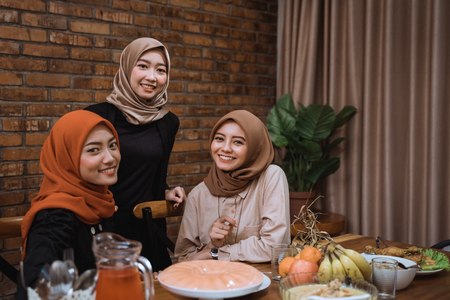 Three young hijab women look at camera while together in the dining roomの写真素材