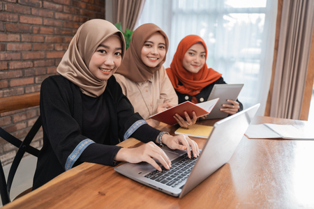 Young beautiful woman veiled smiling looking the camera when sitting with laptop, tablet, and bookの写真素材