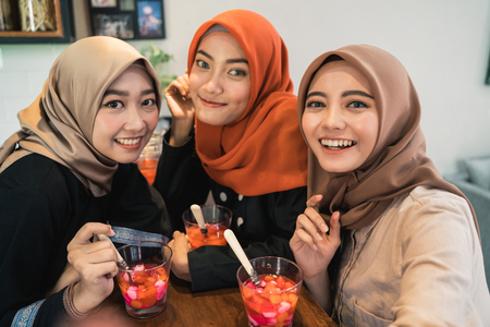 Veiled young women look at camera relaxing using smartphone for selfieの写真素材
