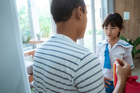 kindergarten student wearing school uniform helped by her fatherの写真素材